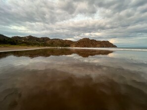 A beach with a calm water surface reflecting the sky and surrounding landscape. - Charming 3-bedroom House Rental in Paquera, Costa Rica (Paquera)