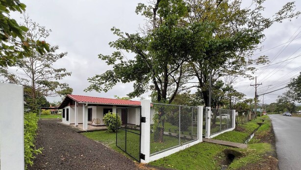 A fenced property with a small building, gravel driveway, and a road in the background. - Charming 3-bedroom House Rental in Paquera, Costa Rica (Paquera)