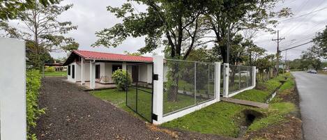 A fenced property with a small building, gravel driveway, and a road in the background.