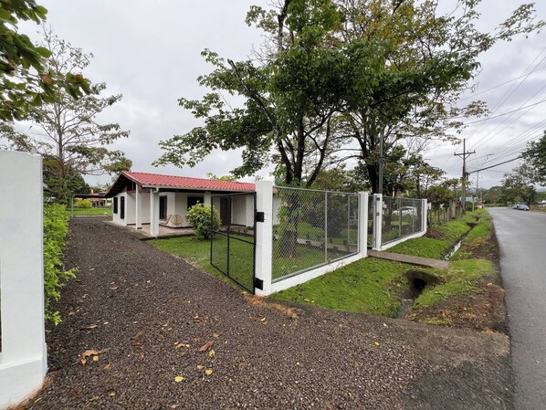 A fenced property with a small building, gravel driveway, and a road in the background. - Charming 3-bedroom House Rental in Paquera, Costa Rica (Paquera)