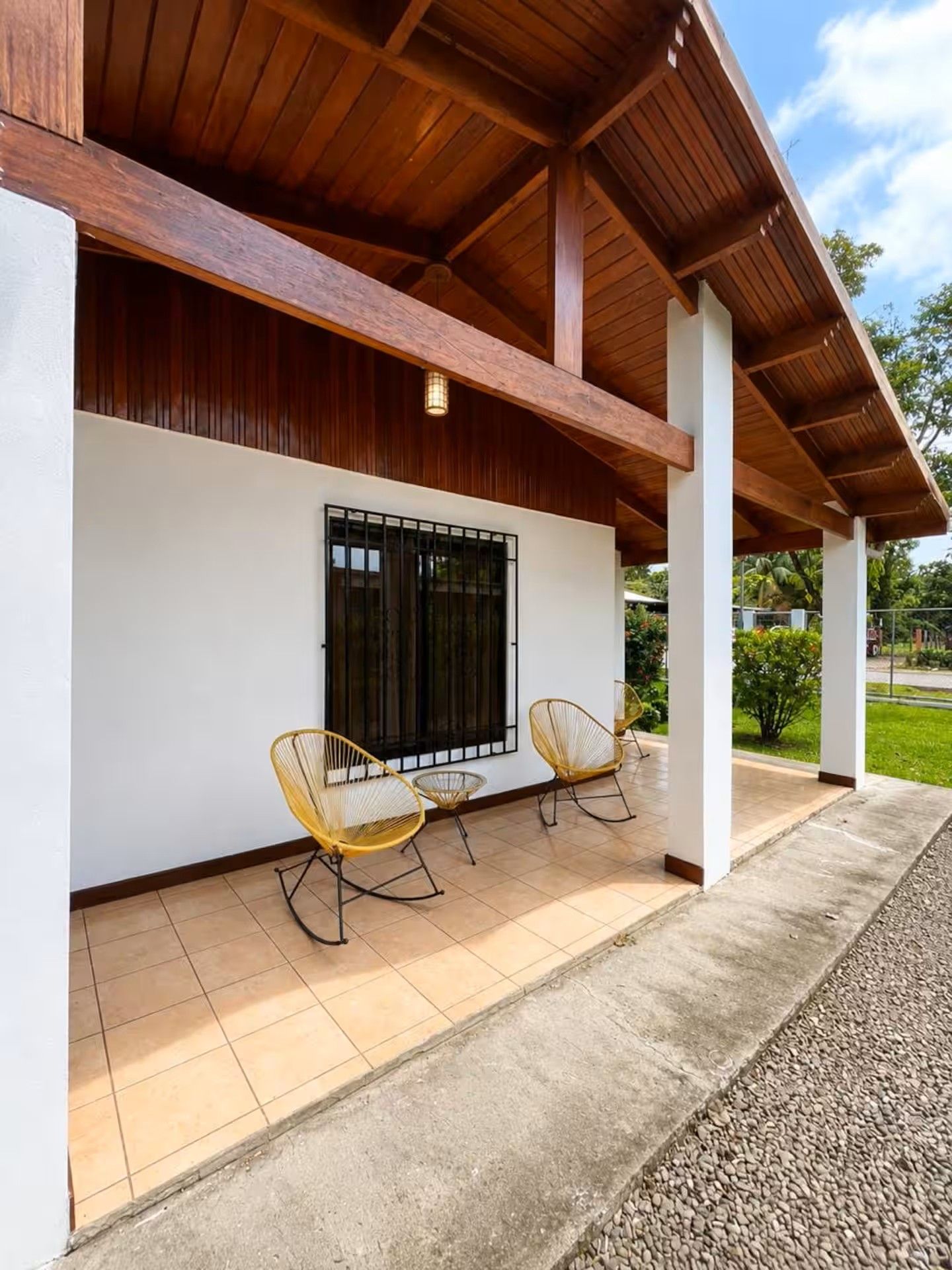 A covered outdoor seating area with two chairs and a window with metal bars.