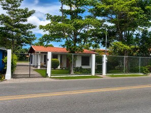 A fenced property with a small building, a paved driveway, and a road with double yellow lines. - Charming 3-bedroom House Rental in Paquera, Costa Rica (Paquera)