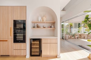A modern kitchen with built-in appliances, wooden cabinetry, and a small seating area with a view of the outdoors. - Burleigh Springs (Pool & Walk to the beach) (Burleigh Heads)