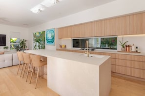 Une cuisine moderne dotée d’un îlot central, de tabourets de bar, de meubles en bois et d’une grande fenêtre offrant une vue sur la verdure.