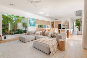 A modern living room with a sectional sofa, a dining area, and a kitchen in the background. - Burleigh Springs (Pool & Walk to the beach) (Burleigh Heads)