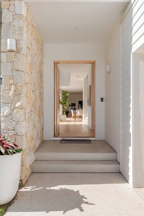 A modern entryway with a stone wall, a wooden door, and a view into a well-lit interior space. - Burleigh Springs (Pool & Walk to the beach) (Burleigh Heads)