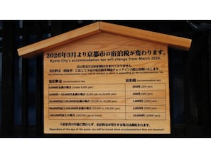 Ein Holzschild mit Informationen zu Änderungen der Kyoto Stadt-Unterkunftssteuer ab März 2026.