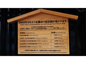Ein Holzschild mit Informationen zu Änderungen der Kyoto Stadt-Unterkunftssteuer ab März 2026.