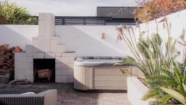 Een terras met een hottub, een stenen open haard en een rieten bank.
