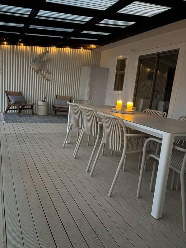 An outdoor dining area with a white table and chairs, a candle on the table, and a wooden deck.