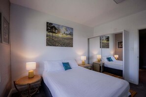 A hotel room with a bed, two bedside tables with lamps, a large mirror, and a painting on the wall.