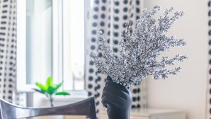A vase with a plant on a table in a room with a modern design, including a patterned curtain and a window with blinds. - Stylish 2BR Apartment Long Stay for 5 (Vienna)