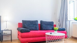 A red sofa with black cushions, a white round coffee table, and a small side table with a lamp. - Stylish 2BR Apartment Long Stay for 5 (Vienna)