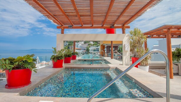 Ein Pool auf dem Dach mit Blick aufs Meer, umgeben von roten Pflanzgefäßen und einer Holzpergola.