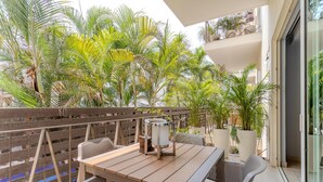 Ein Balkon mit Holztisch und Korbstühlen, umgeben von Blumentöpfen und einem Holzzaun.