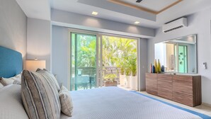 Ein Schlafzimmer mit einem großen Bett, einem Schminktisch, einem Spiegel und einer Glastür, die auf einen Balkon mit Pflanzen führt.