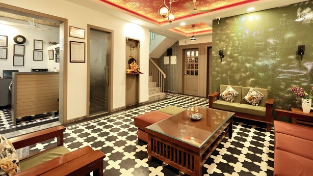 A hotel lobby with a checkered floor, a sofa, a coffee table, and a staircase leading to the upper floor. - OnlyStay Kirpalu Dham - Opp. Prem Mandir, Vrindavan (Vrindavan)
