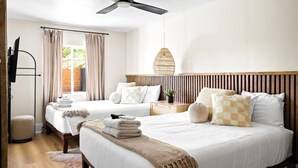 Camera d'albergo con due letti, televisione, ventilatore a soffitto e vista su aree verdi.