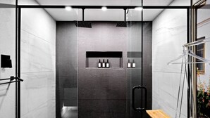 Un'area doccia moderna con porta in vetro, uno sgabello in legno e un portasciugamani.