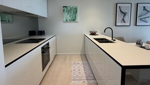 Een moderne keuken met witte kasten, een zwart aanrecht en een houten vloer. Er ligt een vloerkleed in het midden en er hangt kunst aan de muur.