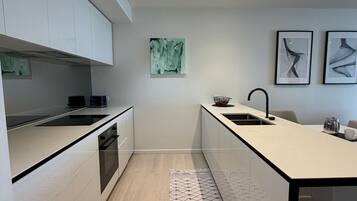 Eine moderne Küche mit weißen Schränken, einer schwarzen Arbeitsplatte und Holzboden. Ein Teppich liegt in der Mitte, und an der Wand hängt ein Kunstwerk.