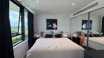 Ein Hotelzimmer mit einem großen Bett, einem Nachttisch, einem Schreibtisch, einem Sessel, einem Fenster mit Vorhängen und einem Bild an der Wand.