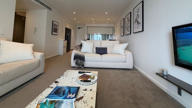 Een moderne woonkamer met een bank, een salontafel met tijdschriften en een televisie aan de muur.