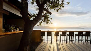 A terrace with chairs overlooking a body of water at sunset, a tree, and a building with a window and potted plants. - 2 bedroom lovely (sta)caravan in Glavotok (Glavotok)