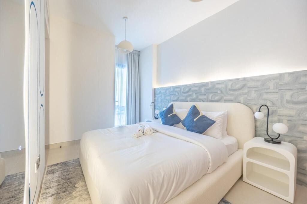 A modern bedroom with a large bed, a nightstand, and a wall-mounted light fixture.