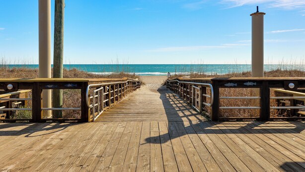 Una pasarela de madera que lleva a la playa, con barandillas y una vista despejada del océano.