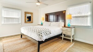 Un dormitorio con cama, lámparas de noche, ventilador de techo y ventana con persianas.