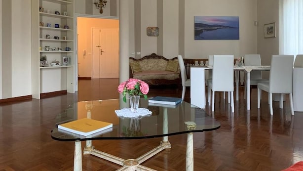 A living room with a glass-top coffee table, a sofa, a dining table with chairs, a bookshelf, and a painting on the wall. - Charming BnB in the Heart of Ravenna in its wonderfull Green! (Ravenna)