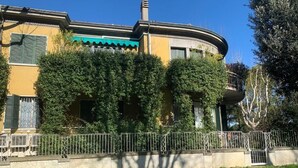 A building with a curved facade, a green awning, and a metal fence in front. - Triple Room Business (Ravenna)