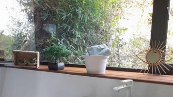 Ein modernes Badezimmer mit schwarzer Ablage, einem weißen Waschbecken und einem Fenster mit Blick auf Grünflächen.