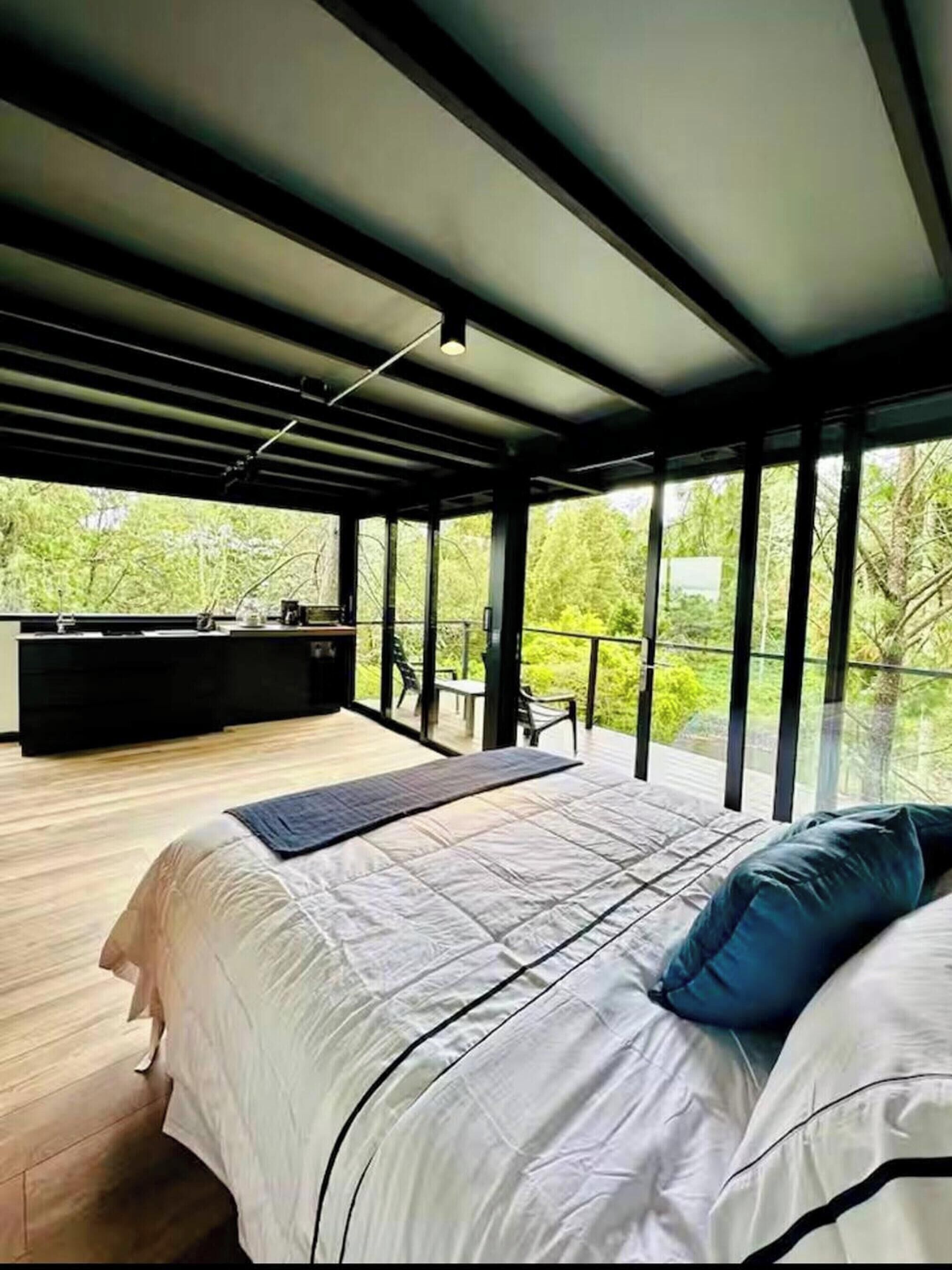Ein modernes Schlafzimmer mit einem großen Bett, einem Schreibtisch und einem Balkon mit Blick auf Grünflächen.