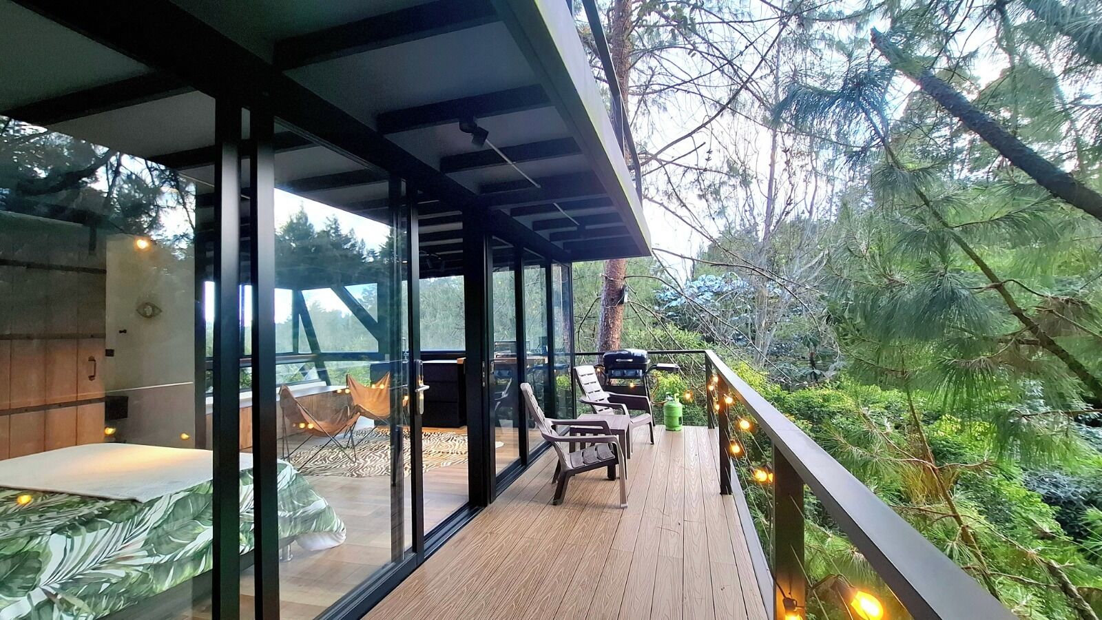 Eine moderne Außenterrasse mit Glaswänden, Holzboden und Gartenmöbeln.