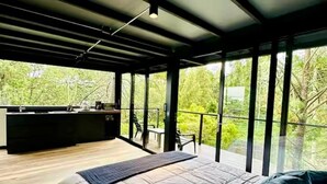 Une chambre moderne avec un grand lit, un bureau et un balcon offrant une vue sur la verdure.