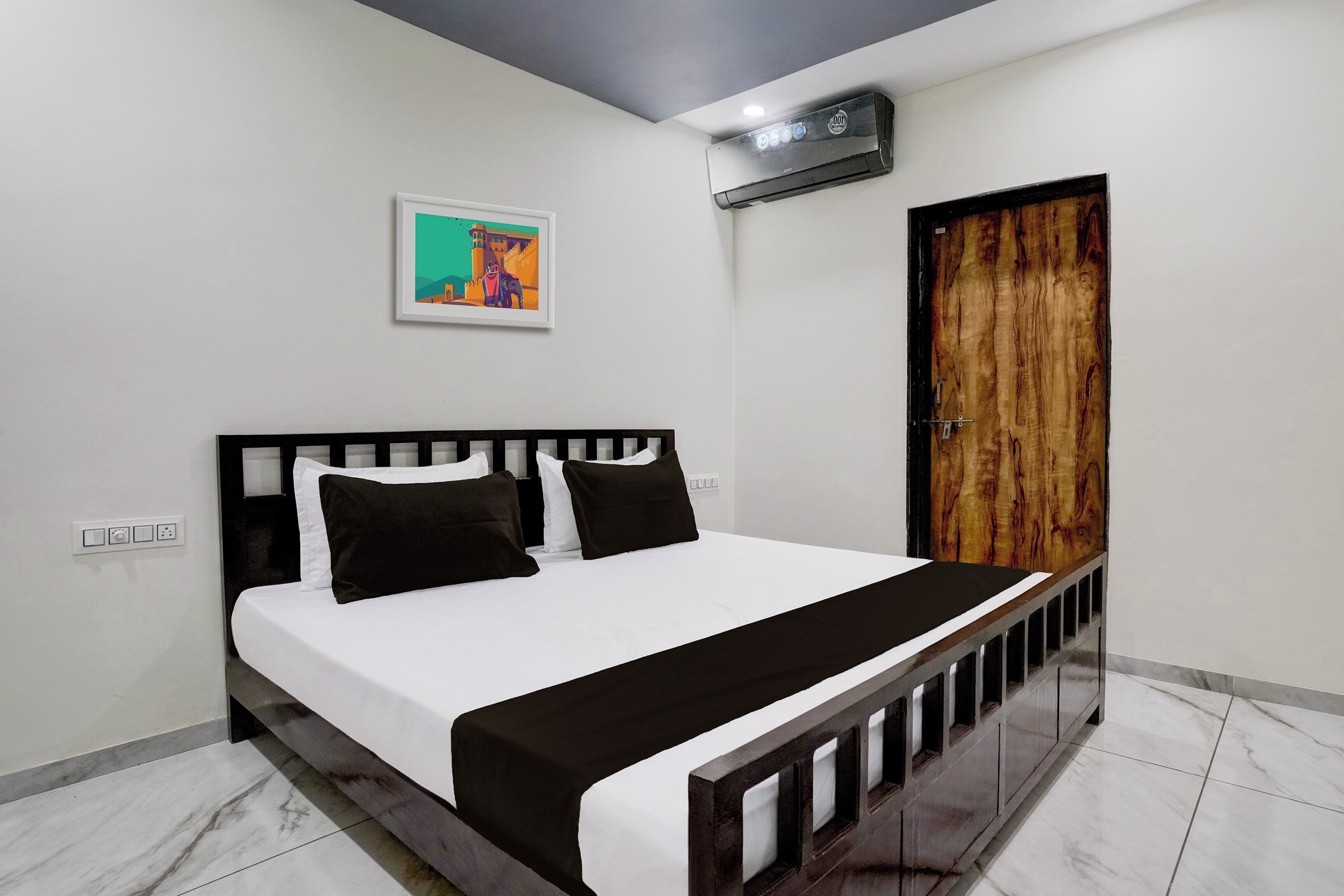 Une chambre à coucher avec un lit, une porte en bois, un climatiseur fixé au mur et un tableau encadré.