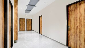 A hallway with wooden doors, a polished marble floor, and recessed lighting. - Hotel Ambika, Vadodara (Waghoriya)