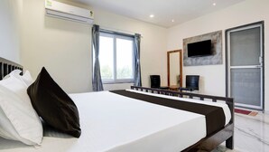 A bedroom with a bed, a TV mounted on the wall, an air conditioning unit, and a sliding door. - Hotel Ambika, Vadodara (Waghoriya)