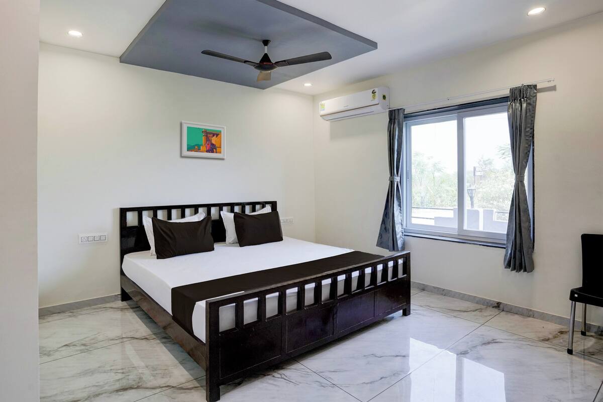 A bedroom with a bed, ceiling fan, air conditioning unit, window with curtains, and a chair.