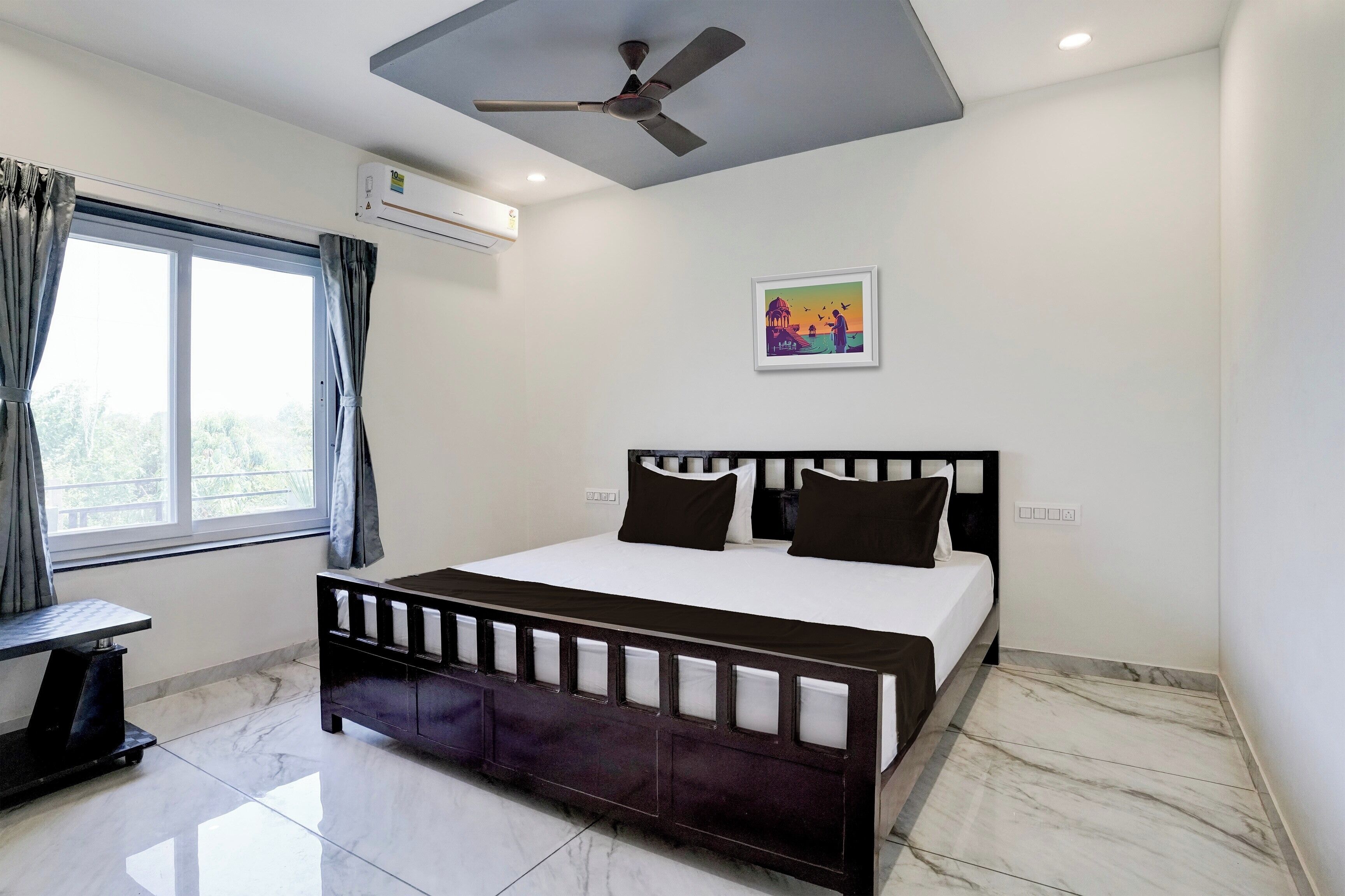 A bedroom with a bed, a ceiling fan, an air conditioner, a window with curtains, and a framed picture on the wall.