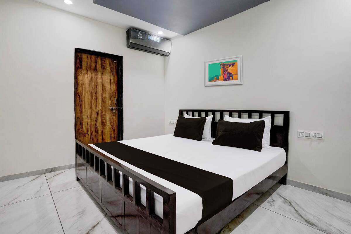 A bedroom with a bed, a wooden door, an air conditioning unit, and a wall-mounted picture.