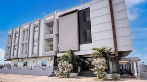 A modern multi-story building with a flat facade, large windows, and a central entrance with steps. - Hotel Ambika, Vadodara (Waghoriya)