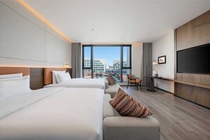 Hotellihuone, jossa on kaksi sänkyä, sohva, televisio ja näkymä rakennuksiin.