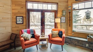 A cozy room with wooden walls, two orange armchairs, a bench, a small table with a lamp, and a view of trees through large windows. - 4-Season Recreation: Secluded Pike River Cabin (Tower)