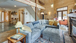 A spacious living area with a large sectional sofa, a fireplace, and a staircase leading to an upper level. - 4-Season Recreation: Secluded Pike River Cabin (Tower)