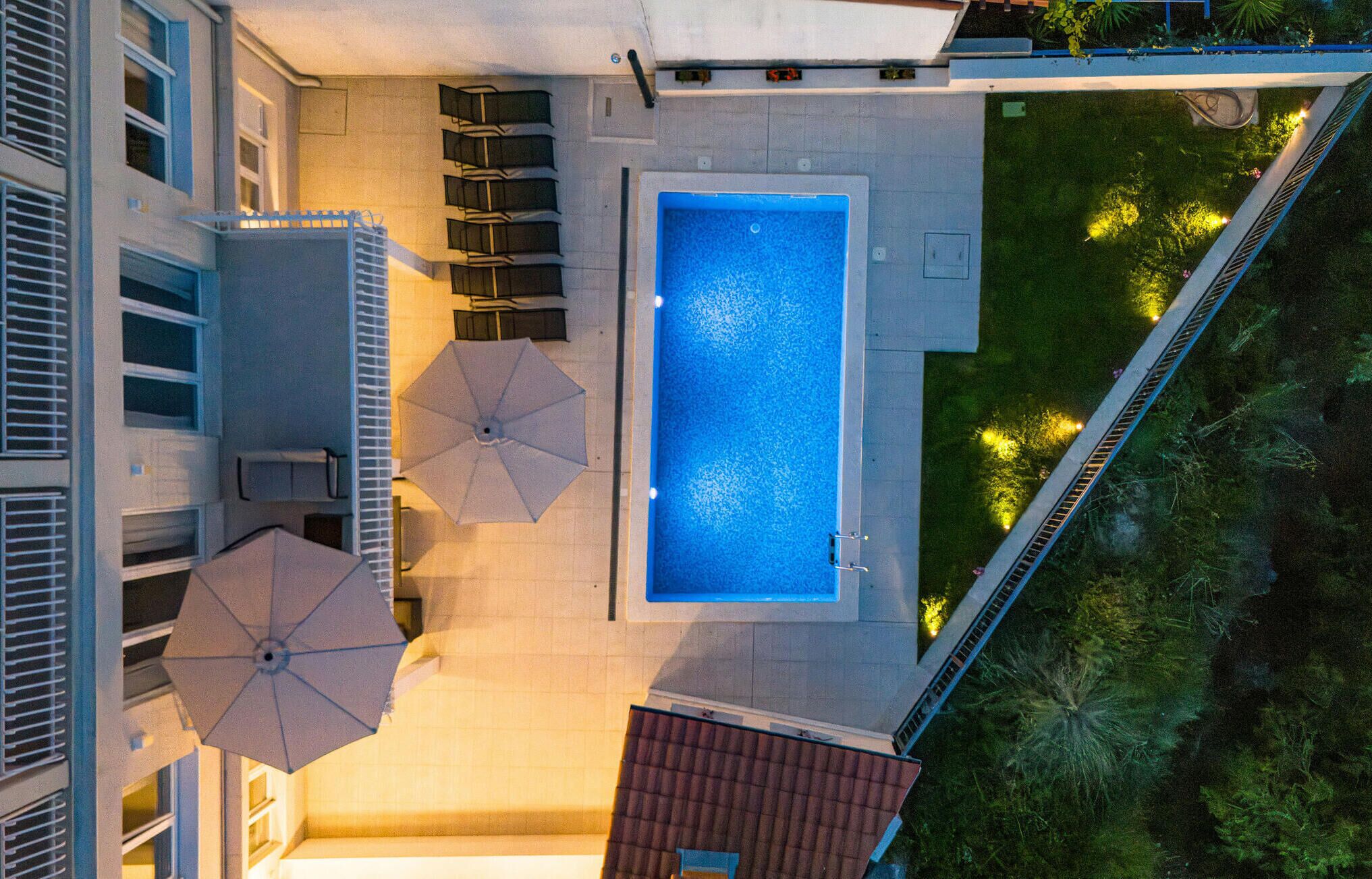 An aerial view of a rooftop swimming pool with a rectangular shape, surrounded by a few umbrellas and seating areas.