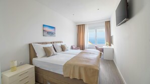 Habitació d'hotel amb un llit gran, escriptori, cadira, televisió i finestra amb vista al mar.