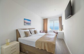 Ein Hotelzimmer mit einem großen Bett, einem Schreibtisch, einem Sessel, einem Fernseher und einem Fenster mit Meerblick.